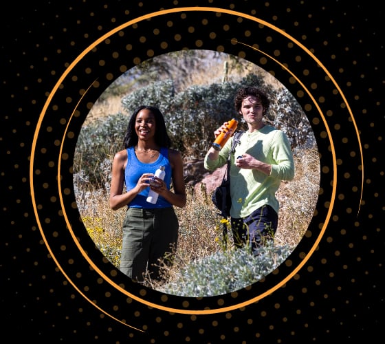 Two hikers standing in a field stopping for a water break to get hydrated.