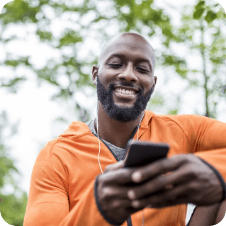 Man in orange running jacket listening to music on his phone with headphones.