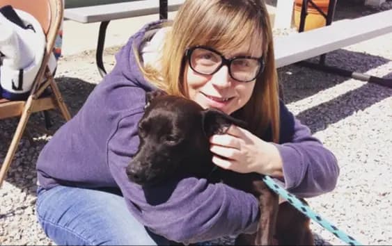 Mujer con suéter morado abrazando a un perro.