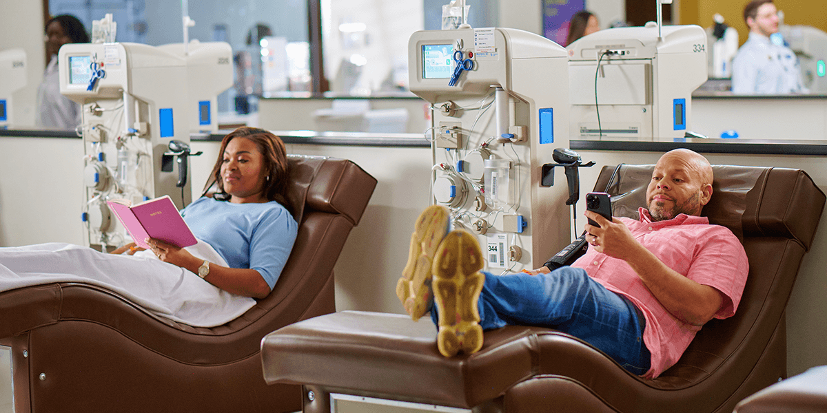 Male donor on phone and Female donor reading book in donation chair